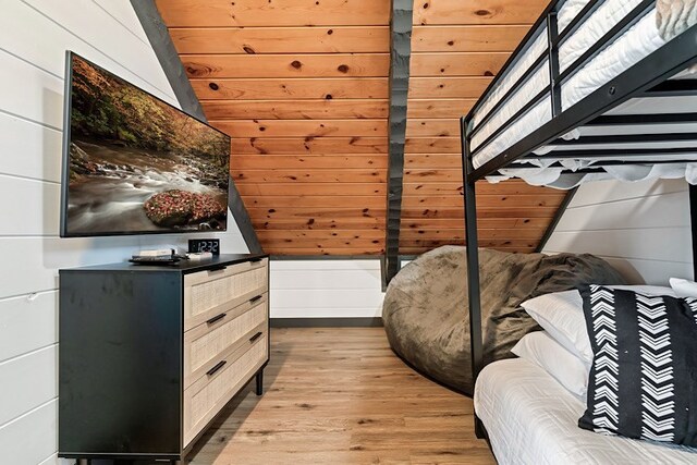 unfurnished bedroom featuring light wood-type flooring, wooden walls, and vaulted ceiling