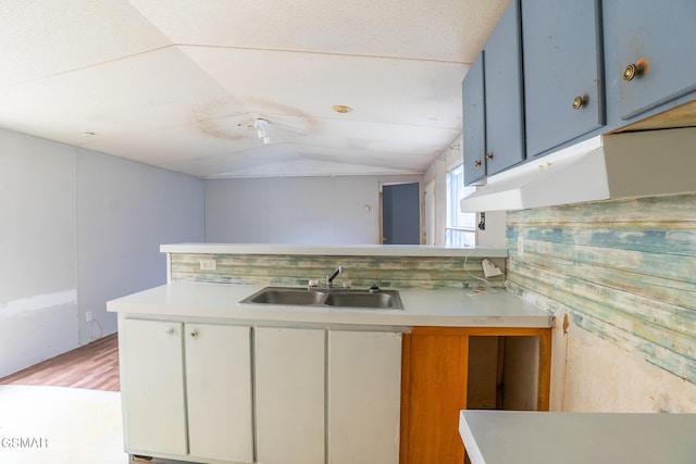 kitchen with light countertops, vaulted ceiling, a peninsula, and a sink