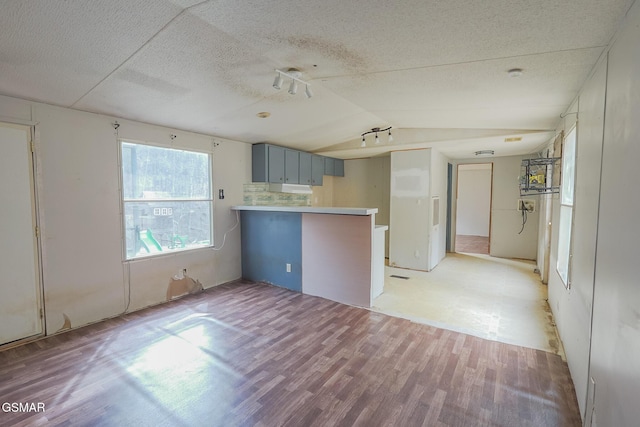 kitchen featuring vaulted ceiling, light wood-style flooring, a peninsula, gray cabinets, and a textured ceiling