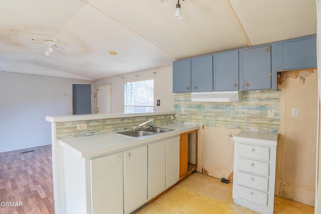 kitchen with light floors, light countertops, lofted ceiling, a peninsula, and a sink