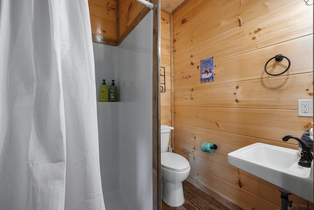 full bath featuring wood walls, a stall shower, toilet, and a sink