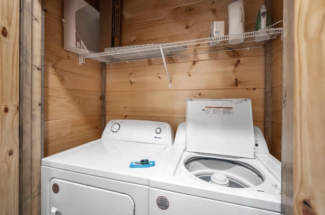 clothes washing area featuring washing machine and clothes dryer, laundry area, and wood walls