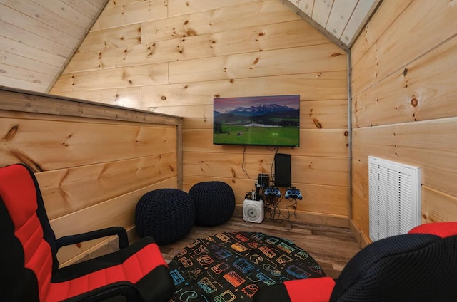 sitting room featuring visible vents, wood walls, lofted ceiling, and wood finished floors