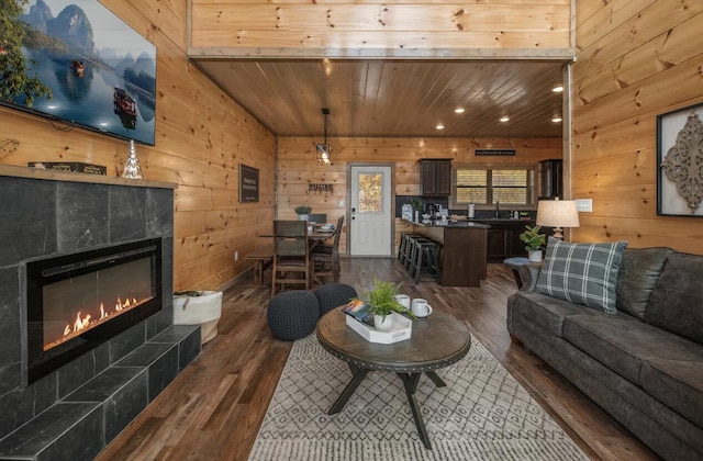 living area with wood ceiling, dark wood-style floors, wood walls, and a tile fireplace