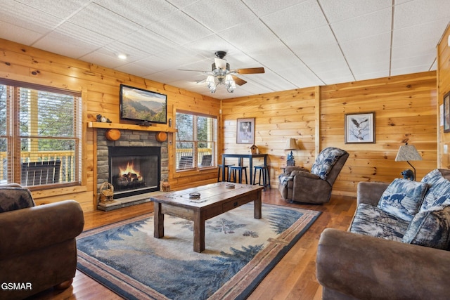 living area with a wealth of natural light, wood walls, a stone fireplace, and wood finished floors