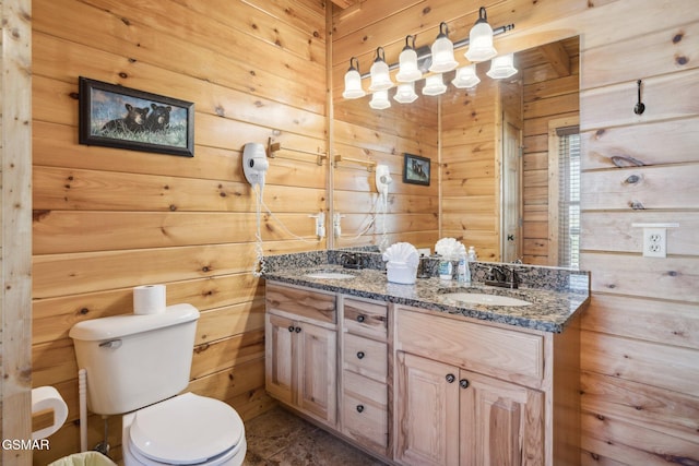 full bathroom featuring double vanity, wood walls, a sink, and toilet