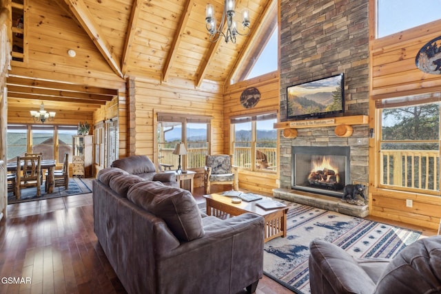 living room with a stone fireplace, wood walls, beam ceiling, and an inviting chandelier