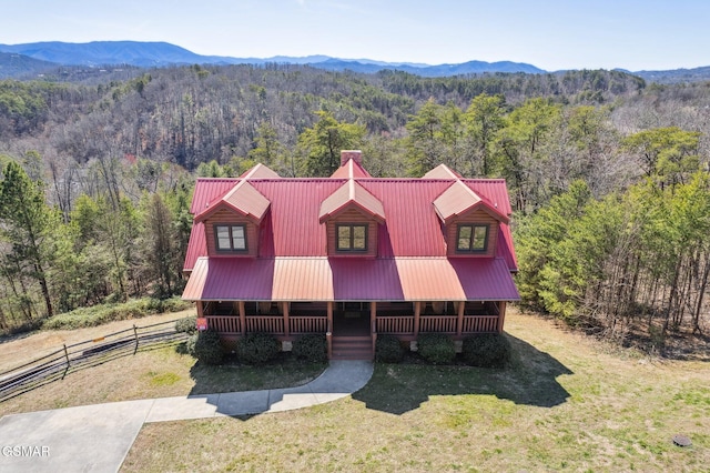 view of front facade with covered porch, fence, metal roof, a wooded view, and a front lawn