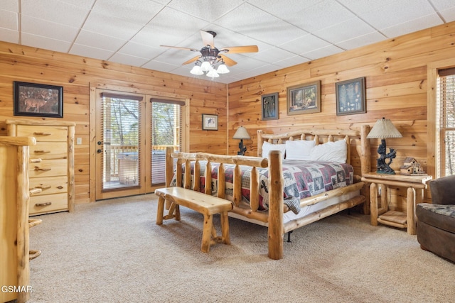 bedroom with wood walls, carpet, a ceiling fan, and access to exterior