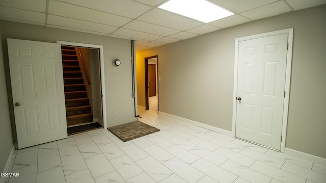 empty room featuring a drop ceiling, marble finish floor, baseboards, and stairs