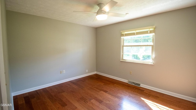 spare room with a textured ceiling, baseboards, dark wood finished floors, ceiling fan, and visible vents