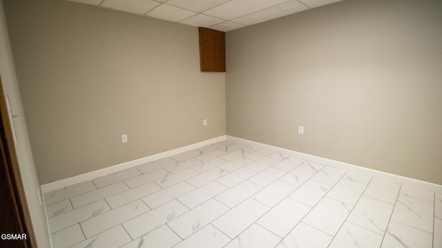 empty room featuring baseboards, marble finish floor, and a drop ceiling