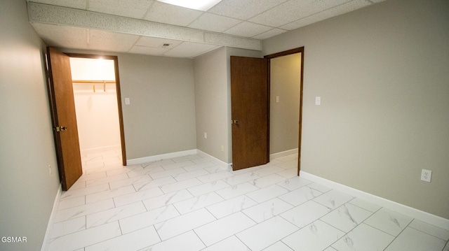 unfurnished bedroom with a closet, a paneled ceiling, baseboards, marble finish floor, and a spacious closet