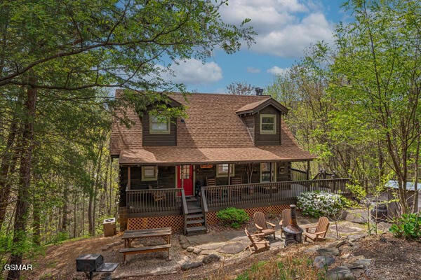chalet / cabin featuring roof with shingles, a porch, and an outdoor fire pit