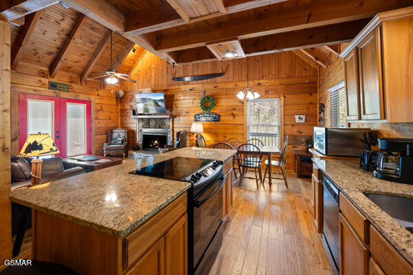 kitchen featuring light wood-style flooring, vaulted ceiling with beams, wooden ceiling, a stone fireplace, and appliances with stainless steel finishes