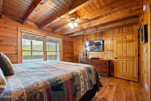 bedroom with wooden walls, beamed ceiling, and light wood finished floors