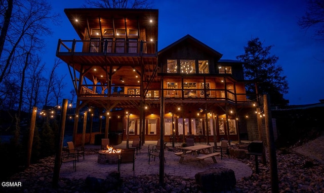 back house at twilight with a balcony, a patio area, and a fire pit