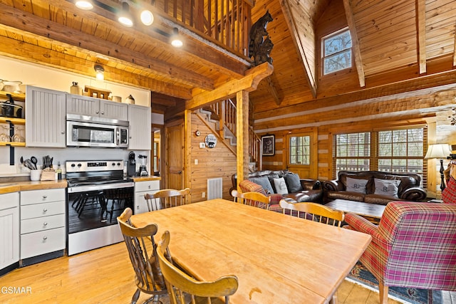 dining room featuring wooden walls, beam ceiling, stairs, wood ceiling, and light wood-style floors