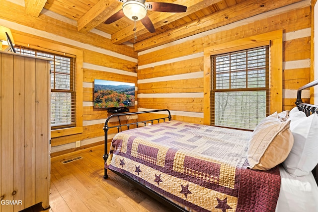 bedroom featuring visible vents, beamed ceiling, wood walls, wood ceiling, and wood-type flooring