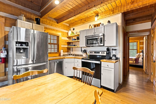 kitchen with beamed ceiling, open shelves, light wood-style floors, appliances with stainless steel finishes, and wooden ceiling