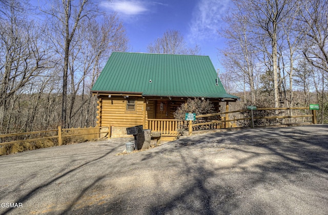 view of front of house featuring driveway, a porch, fence, metal roof, and log siding