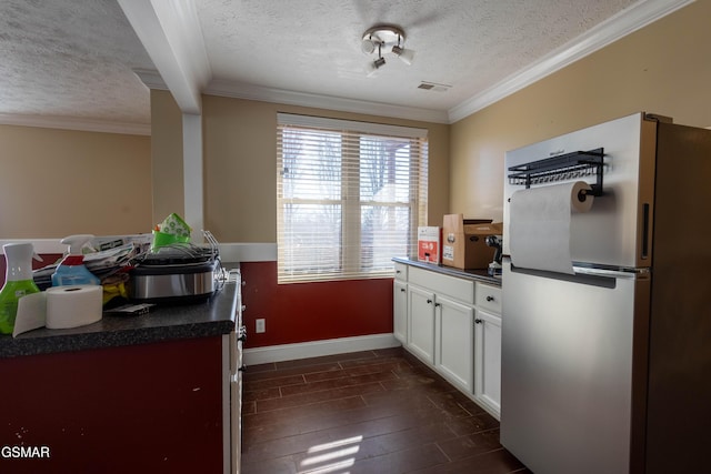 kitchen with a textured ceiling, white cabinetry, crown molding, and stainless steel refrigerator