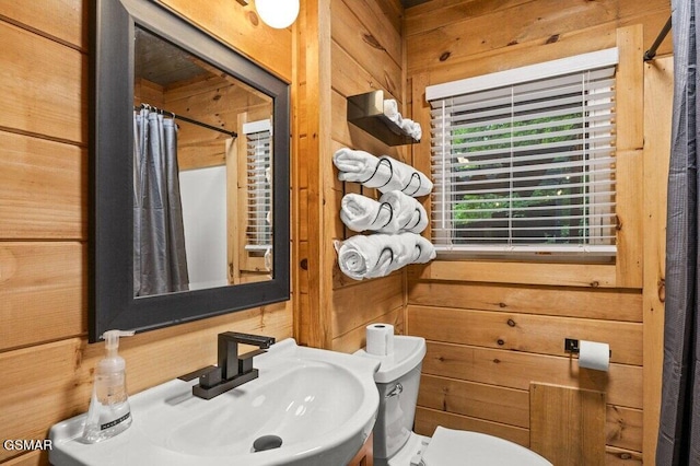 bathroom featuring curtained shower, toilet, sink, and wooden walls