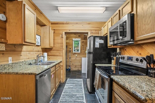 kitchen featuring wooden walls, light stone counters, sink, and appliances with stainless steel finishes