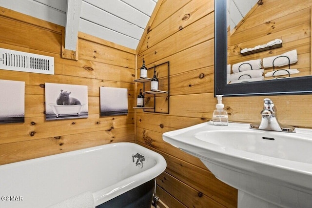 bathroom featuring sink, vaulted ceiling, a tub, and wood walls