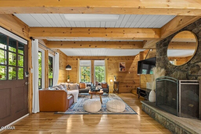 living room with beamed ceiling, wood walls, a stone fireplace, and light hardwood / wood-style flooring