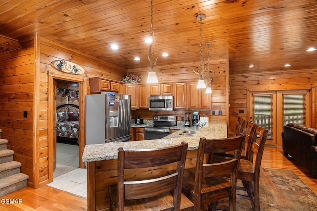 kitchen with hanging light fixtures, light hardwood / wood-style flooring, light stone countertops, kitchen peninsula, and stainless steel appliances