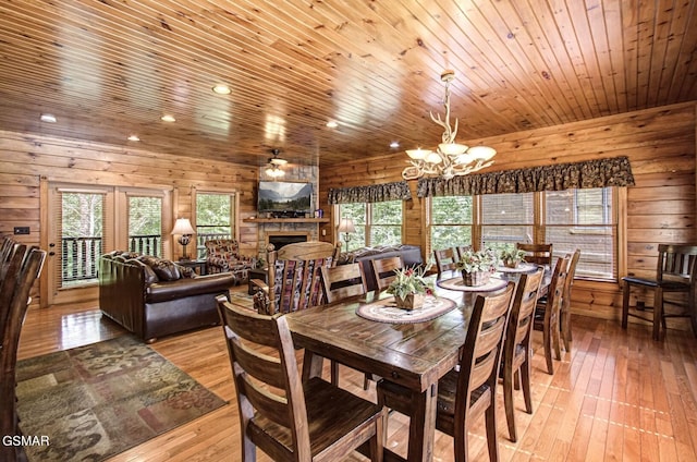 dining space featuring a stone fireplace, wood walls, a notable chandelier, and light wood-type flooring