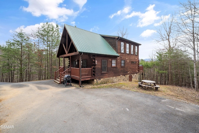 view of home's exterior with covered porch, metal roof, log exterior, and driveway