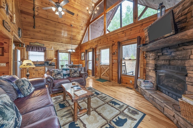 living area featuring high vaulted ceiling, a fireplace, wooden walls, and light wood finished floors