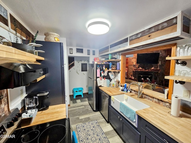 kitchen with wood counters, built in shelves, stainless steel appliances, sink, and light hardwood / wood-style flooring