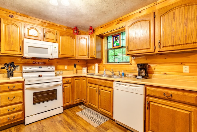 kitchen featuring a textured ceiling, white appliances, wooden walls, sink, and light hardwood / wood-style floors