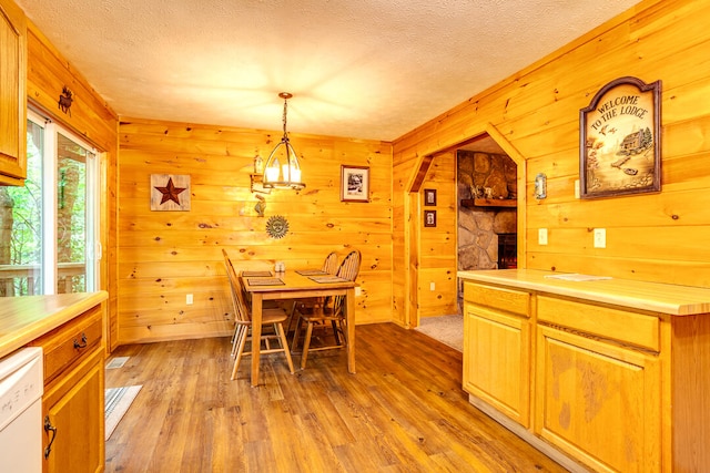 dining room with wood walls, light hardwood / wood-style floors, a stone fireplace, and a textured ceiling