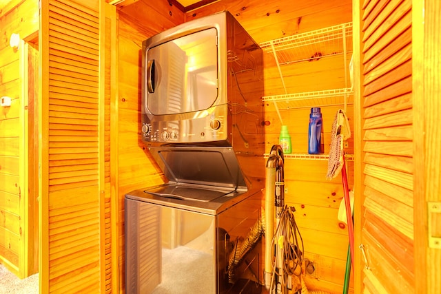 clothes washing area with wood walls, stacked washer and dryer, and carpet