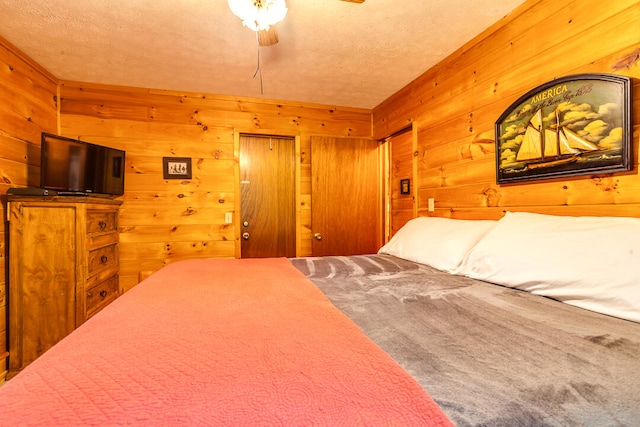 bedroom with ceiling fan, wood walls, and a textured ceiling