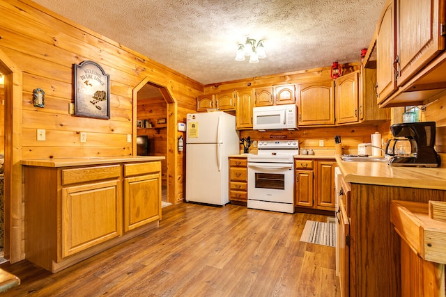 kitchen with wood walls, white appliances, sink, a textured ceiling, and light hardwood / wood-style floors