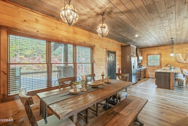 dining space featuring light hardwood / wood-style flooring, wood ceiling, a notable chandelier, and wood walls