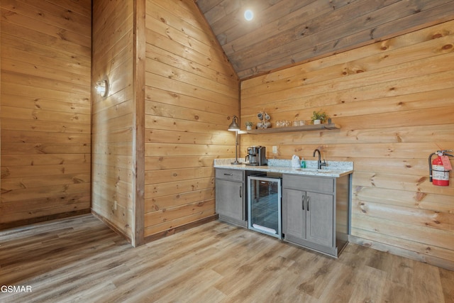 bar with light wood-type flooring, gray cabinets, wine cooler, and wood walls