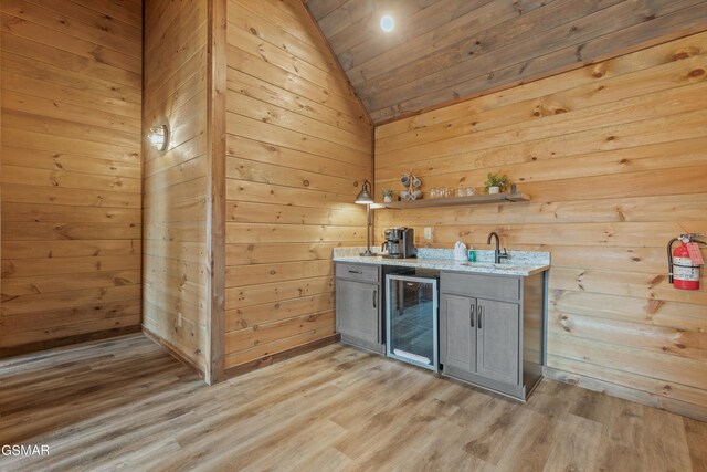 bar with light wood-type flooring, gray cabinets, wine cooler, and wood walls