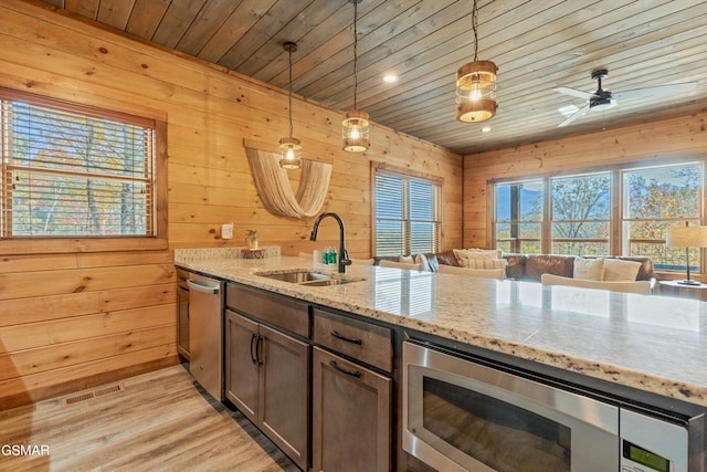 kitchen with light stone counters, wooden walls, pendant lighting, and appliances with stainless steel finishes