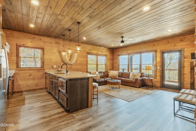 kitchen featuring light stone counters, wood ceiling, hanging light fixtures, stainless steel microwave, and wood walls