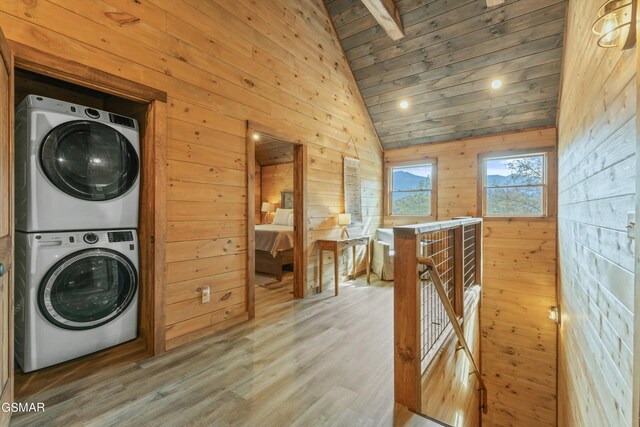 clothes washing area featuring wood-type flooring, stacked washing maching and dryer, wooden walls, and wood ceiling