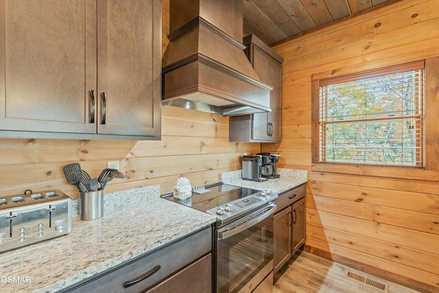 kitchen with stainless steel electric stove, wood walls, light stone countertops, and custom range hood