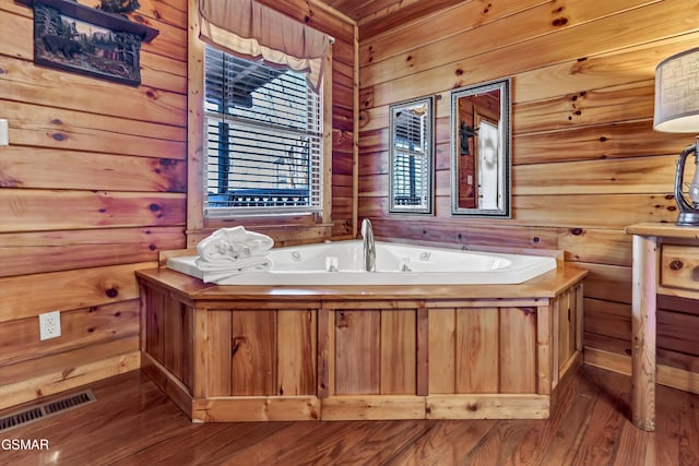 bathroom featuring a garden tub, wooden walls, visible vents, and wood finished floors