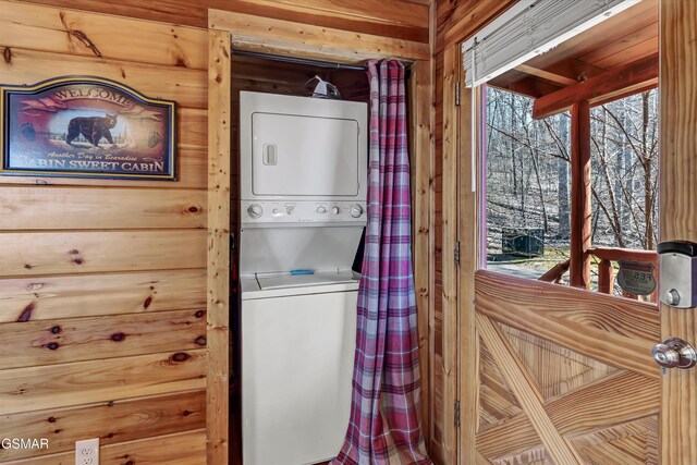 laundry room featuring a wealth of natural light, stacked washer / drying machine, laundry area, and wooden walls