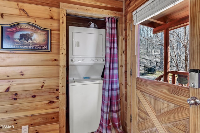 laundry area featuring laundry area, stacked washing maching and dryer, wooden walls, and a healthy amount of sunlight